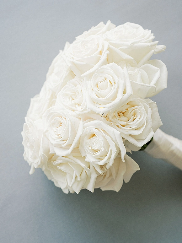 White rose bouquet all white bridal bouquet with tightly arranged blooms, wrapped handle and visible stems resting on a gray surface