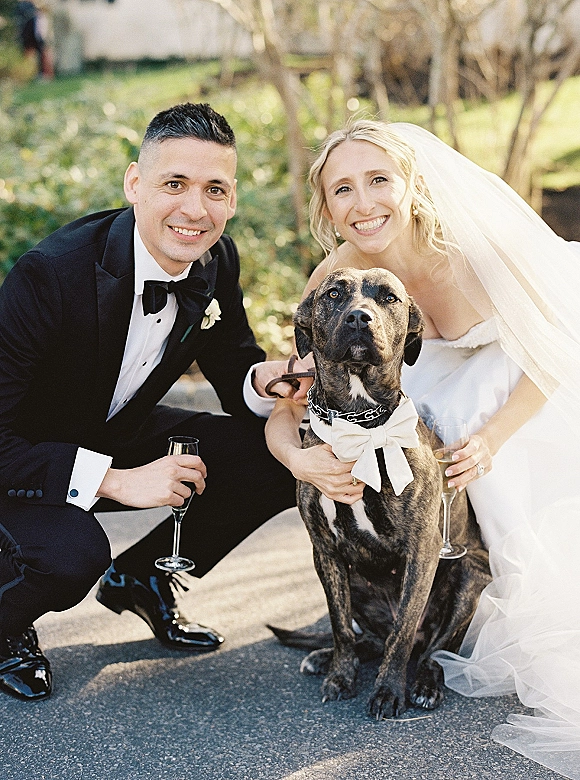 Couple portrait of bride and groom with dog, bride in veil and strapless dress, groom in black tuxedo, on a garden path