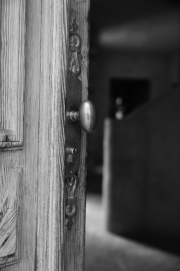 Wedding door detail showing a wood door with vintage door knob, ornate plate and keyhole, opening into a softly blurred interior hallway