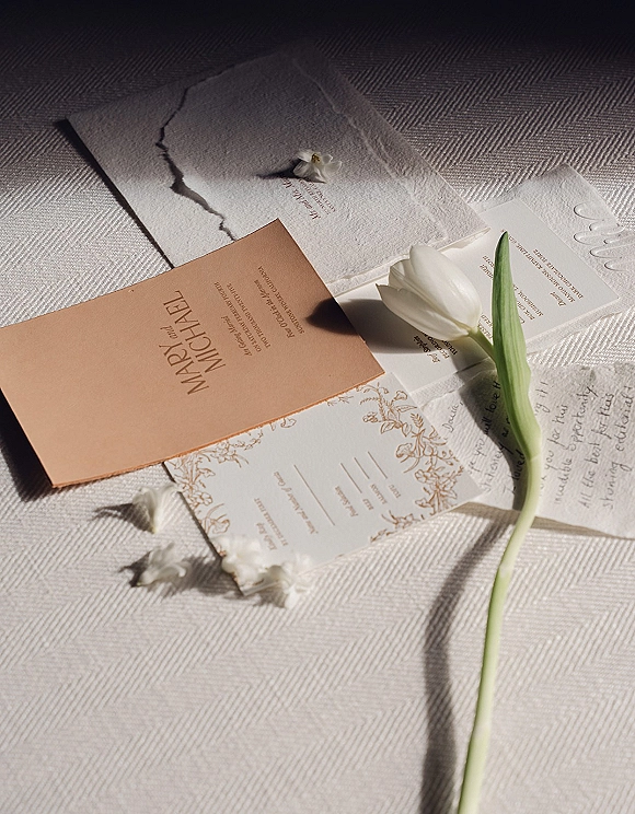 Invitation suite with wedding invitation flat lay on a linen tablecloth, featuring deckle edge paper, blush card, calligraphy, and a white tulip