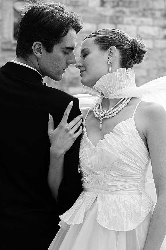 Wedding couple portrait in black and white, bride and groom close up touching foreheads, bride in strapless dress beside a stone wall