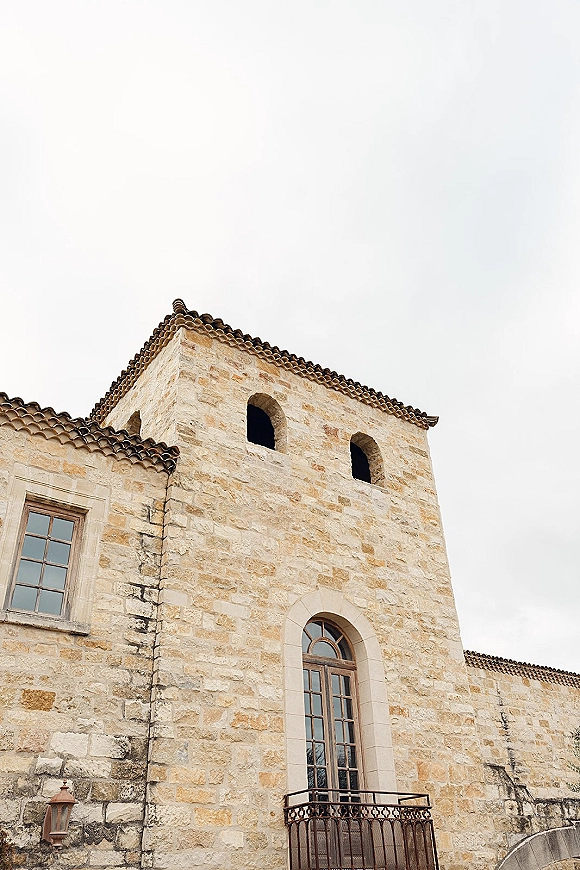 Wedding venue exterior with terracotta roof tiles and arched windows on a stone facade, featuring balcony railing and lantern against the sky