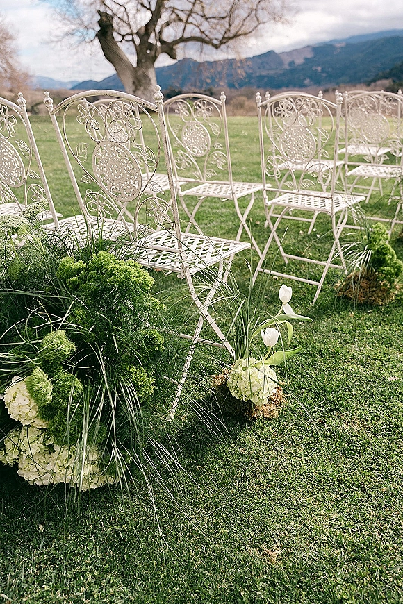 Ceremony seating with outdoor ceremony chairs in neat lawn rows, accented by low hydrangea and tulip florals, mountains beyond under clouds