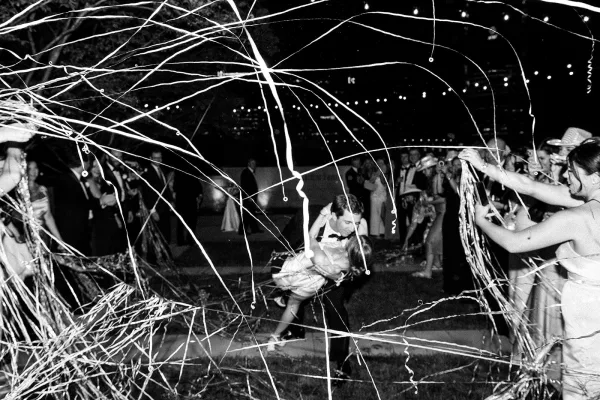 Wedding exit as the bride and groom make their way through a streamer wedding send off beneath string lights under the night sky.