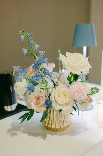 Wedding centerpiece of pastel wedding flowers with airy blue and blush blooms, accompanied by a glowing votive candle for a romantic touch
