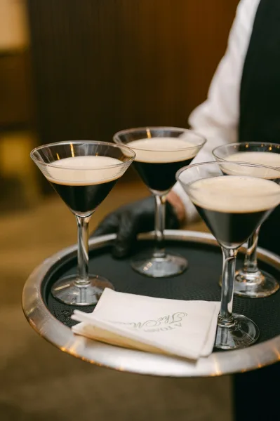 Espresso martini served during a wedding cocktail hour, gleaming on a cocktail tray in a warmly lit indoor venue with rich wood paneling.