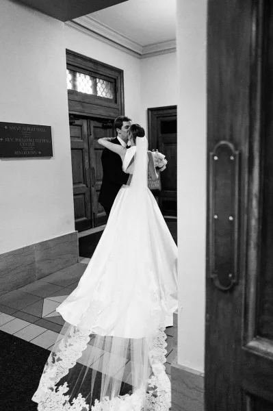 Wedding kiss portrait as the bride and groom embrace beneath a lace veil, framed by wooden doors along a quiet hallway.