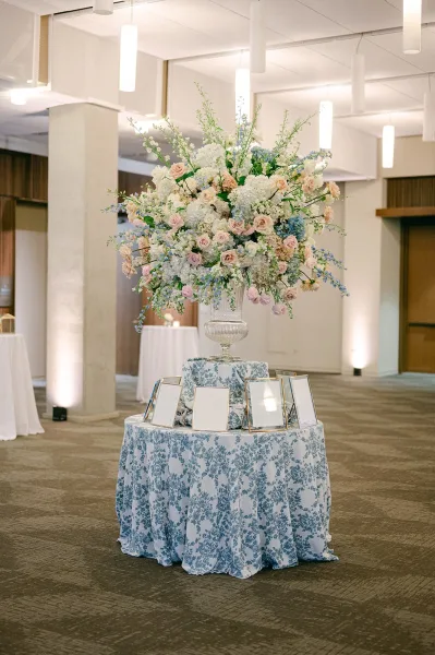 Seating chart display featuring a framed seating chart on a round table draped in patterned table linen in an indoor venue with pendant lights.