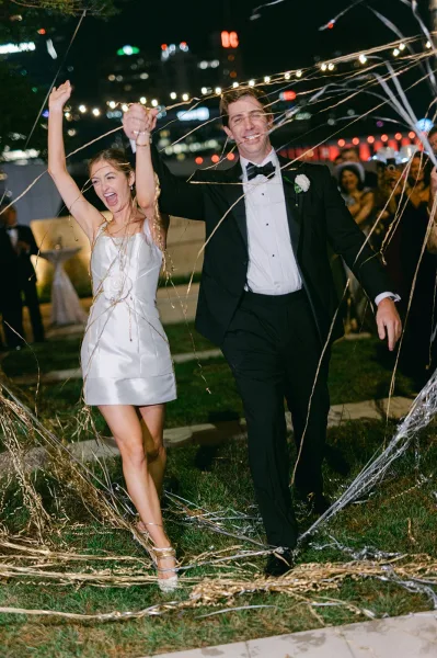 Wedding exit with a streamer send off as newlyweds walk hand in hand through metallic streamers under city lights.