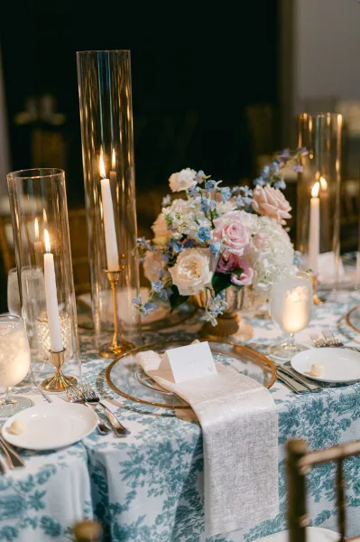 Reception tablescape, a blue floral tablescape set with taper candles, glowing softly against a dark wall indoors