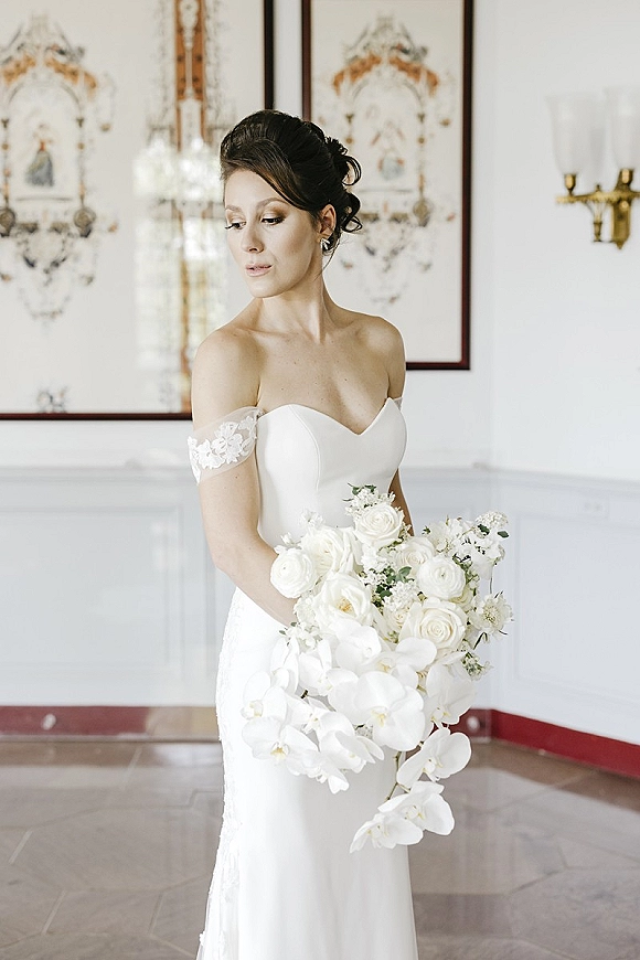 Bridal portrait of a bride in a strapless wedding dress holding a white rose bouquet, posed indoors against white wall paneling