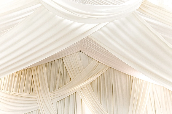 Ceiling drapery decor with wedding tent ceiling draping, featuring soft white fabric swags and a pleated liner across the reception tent ceiling