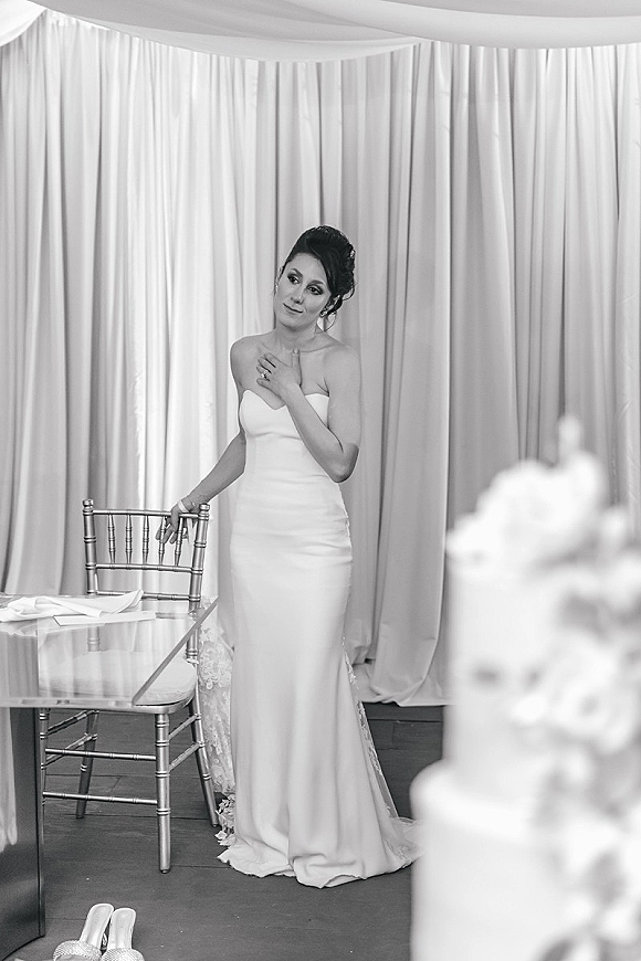 Bridal portrait in black and white of a bride in a strapless gown with lace train, leaning on a chiavari chair in a draped tent