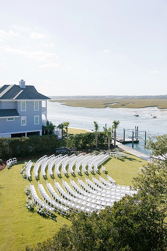 Outdoor ceremony setup with waterfront wedding ceremony seating, white folding chairs in a semicircle on a lawn by a dock and marsh view