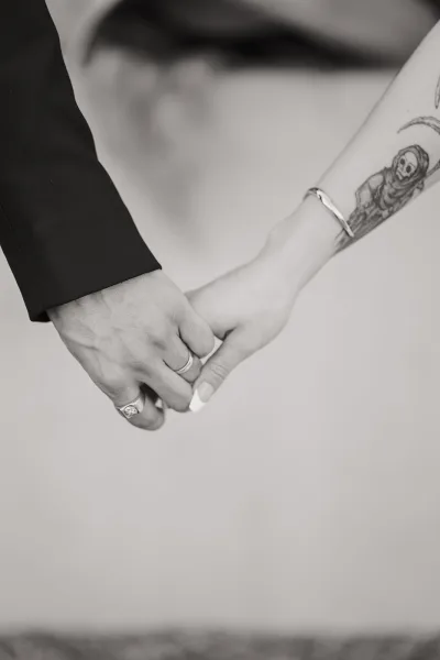 Holding hands photo of newlyweds, wedding hand holding with intertwined fingers, wedding bands and engagement ring against a plain backdrop