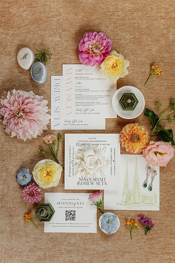 Wedding invitation suite flat lay with menu and RSVP cards, monogram wax seals, rings and emerald earrings on linen backdrop