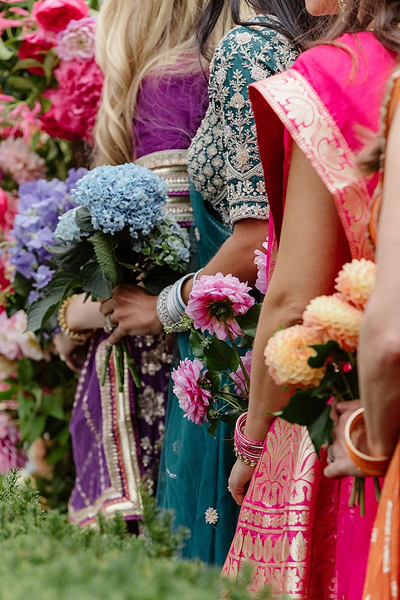 Bridesmaids bouquets held by saree-clad bridesmaids, mixed colorful blooms with bangles visible against blurred garden greenery