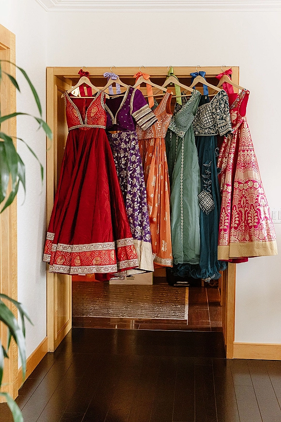 Bridesmaid dresses in a bridesmaid dress lineup on wooden hangers, embroidered with colorful ribbons, hanging in a hallway doorway