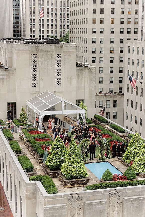 Rooftop wedding ceremony with a rooftop ceremony setup under a white tent, floral arch and aisle chairs beside a pool with city buildings behind