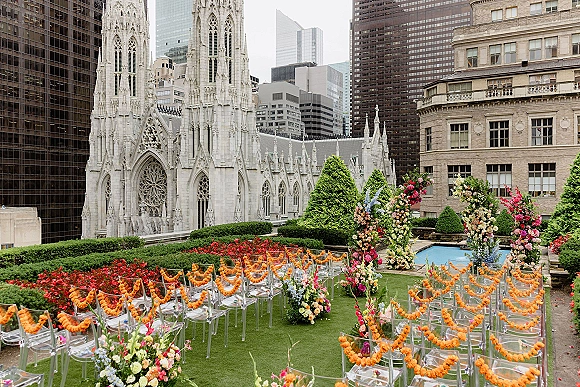 Ceremony setup for a rooftop wedding ceremony with clear acrylic chairs and marigold garlands lining a petal-strewn aisle by the pool