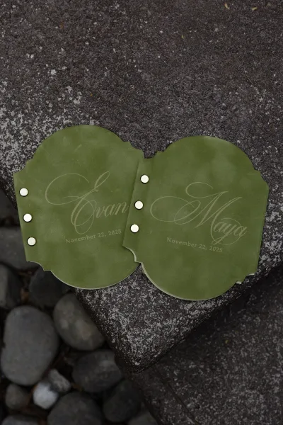 Wedding invitations with green wedding invitation cards in calligraphy lettering, layered with metal brads on a stone surface with pebbles