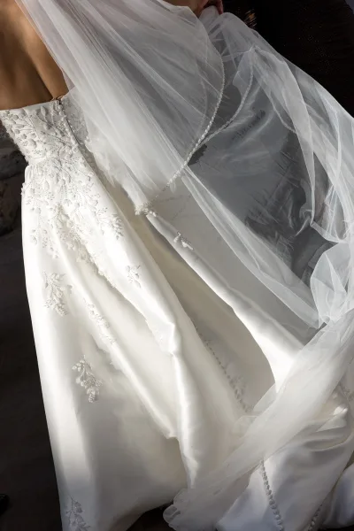 Wedding dress detail showing a strapless lace wedding dress bodice with beading and pearl-trim tulle veil against dark upholstery