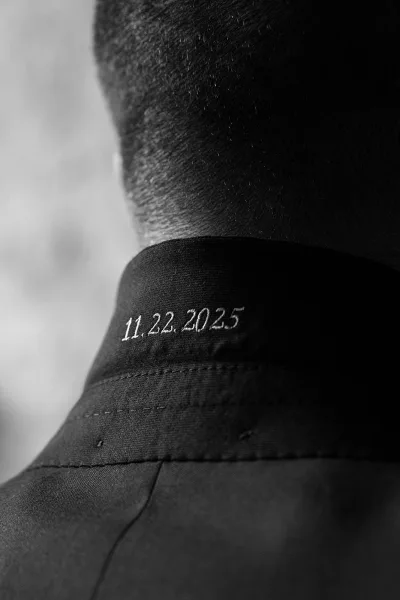 Custom wedding suit with an embroidered wedding date stitched inside the jacket collar, close-up on the groom’s neck against a blurred wall