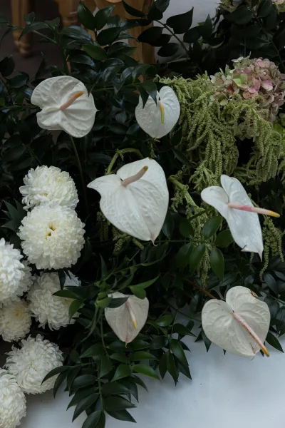 Wedding floral arrangement with anthurium wedding flowers, white mums, blush hydrangea, and greenery foliage on a clean white surface