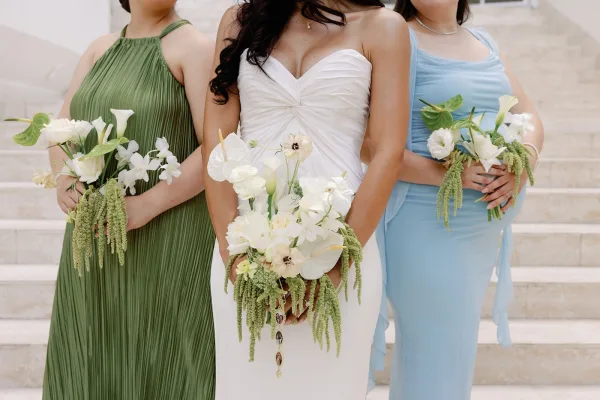 Bride and bridesmaids in mismatched bridesmaid dresses pose on a stone staircase, holding white and green bouquets.