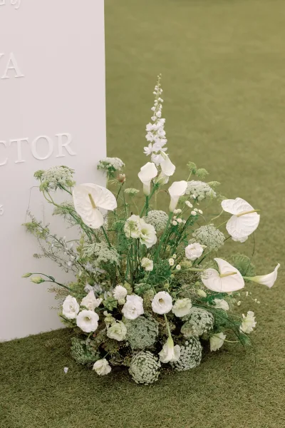 Welcome sign flowers framing a wedding welcome sign with white anthurium, arranged asymmetrically around modern white signage.