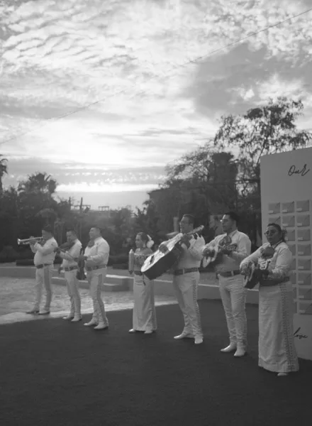 mariachi wedding band performing live wedding music in charro suits on a stone patio as a sunset sky glows above tree-lined lawns.