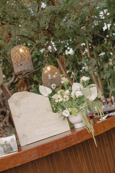 Wedding bar sign with a signature drink sign, styled beside a small disco ball on a wood bar counter set against lush garden greenery.