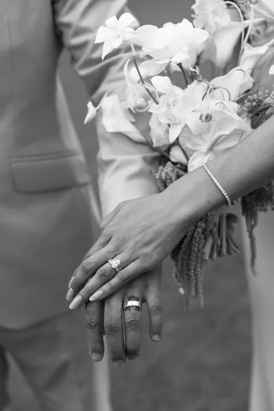 Wedding rings close-up on hands resting against an orchid bouquet, polished bands and fine details captured clearly.