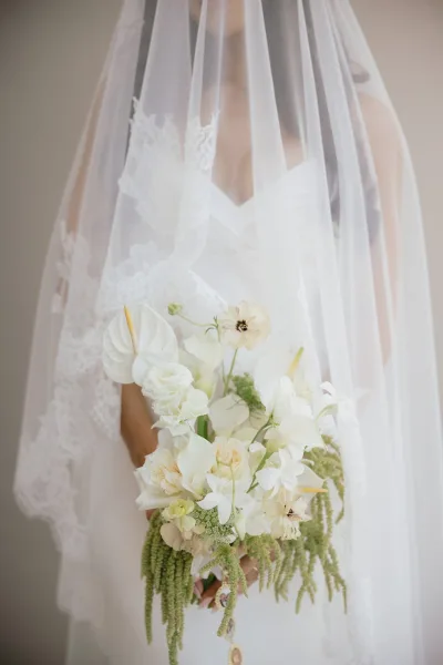 Bouquet close-up of a bridal bouquet with white orchids, roses, and anthurium, its soft textures glimpsed beneath a delicate lace veil.