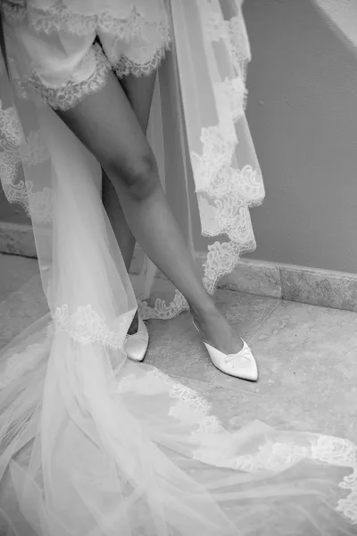 Bridal shoes with pointed toes rest beside a lace veil, an elegant getting-ready detail before the ceremony.