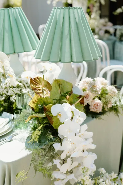 Reception tablescape with a wedding table lamp centerpiece featuring a mint green pleated shade, orchids and blush roses on an outdoor patio table