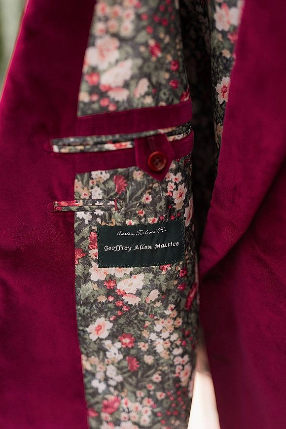 Groom suit detail with floral suit lining revealed inside a burgundy jacket, showing contrast pocket trim, button, and personalized label