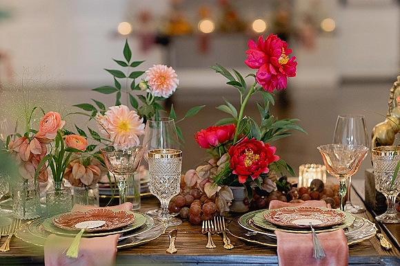 Reception tablescape with a colorful wedding tablescape of peonies and dahlias, bud vases, grapes, blush napkins, and candlelight on wood table