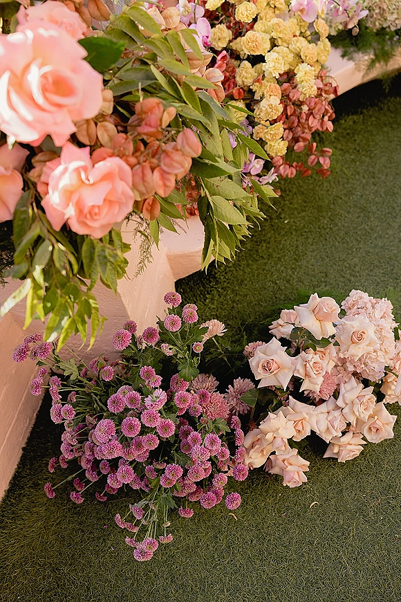 Wedding floral arrangement on a white pedestal stand with pastel roses, hydrangeas and mums, set on a grass lawn with hanging garland