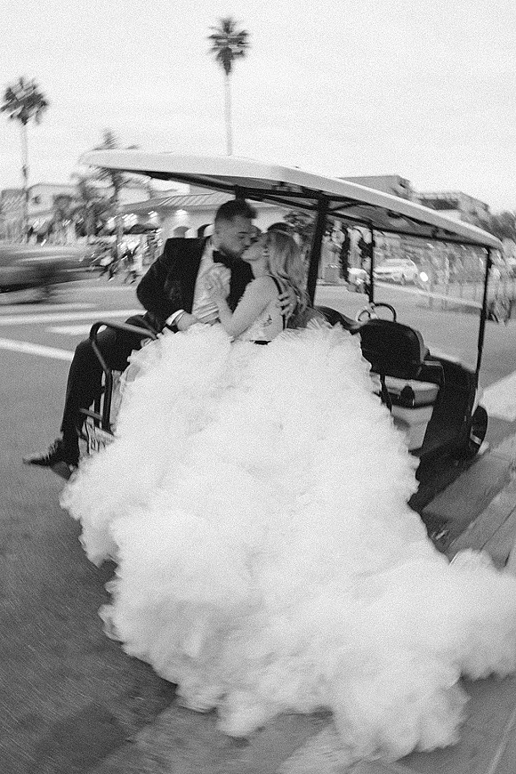 Wedding kiss portrait of bride and groom kissing in a golf cart, her ruffled tulle skirt billowing on a palm-lined street