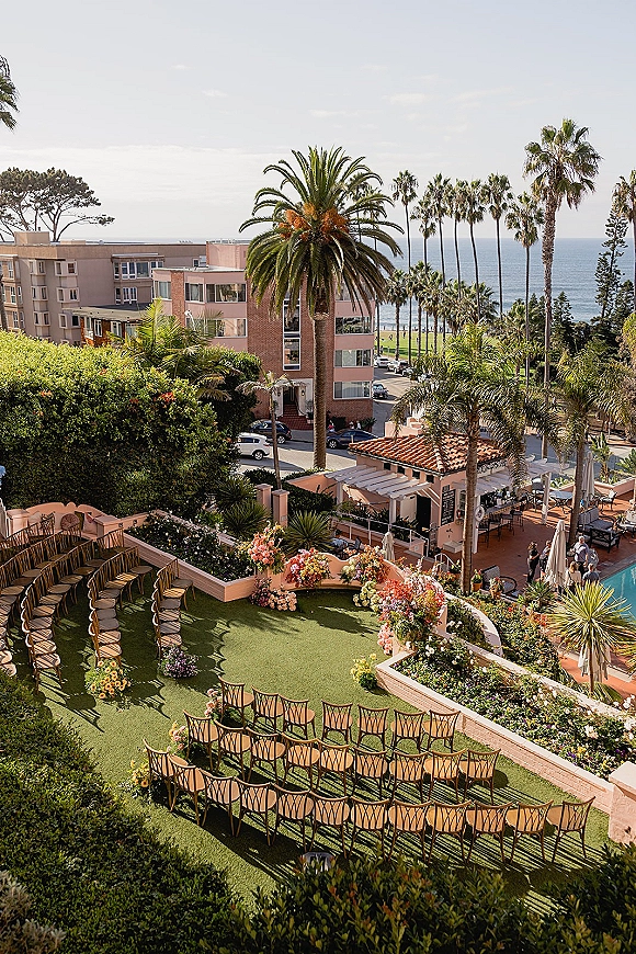 Ceremony setup with outdoor wedding ceremony seating in a semi-circle around a curved aisle, framed by floral entrance accents and ocean-view palms