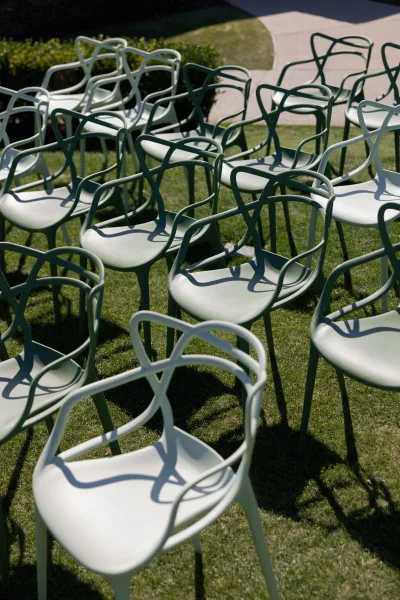 Ceremony seating with outdoor ceremony chairs in sage green, arranged on a grass lawn beside a curved concrete walkway and hedges