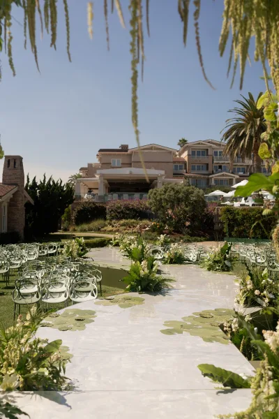 Ceremony aisle design with a white aisle runner wedding, lined with ground florals, greenery and lily pads on a resort lawn under palm trees