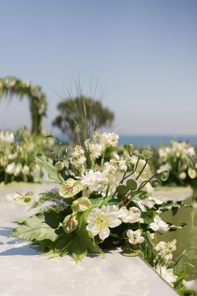 Ceremony aisle flowers in white and green line the lawn leading to a tropical floral arch, with ocean horizon and blue sky beyond