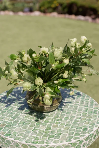 Wedding centerpiece with green and white centerpiece of white flowers and greenery in a round glass vase on a patterned table outdoors