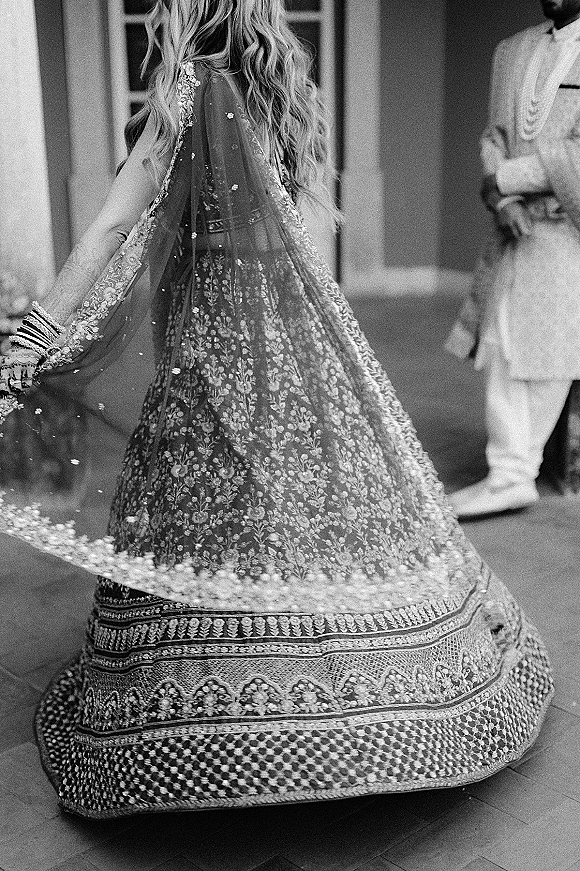 Bridal lehenga twirl as the bride spins, embroidered skirt and dupatta flowing, with bangles and mehndi in a columned courtyard