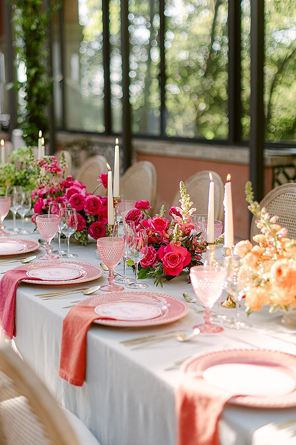 Reception tablescape with wedding table decor, pink rose and snapdragon centerpieces, taper candles, and pink glass goblets by large windows