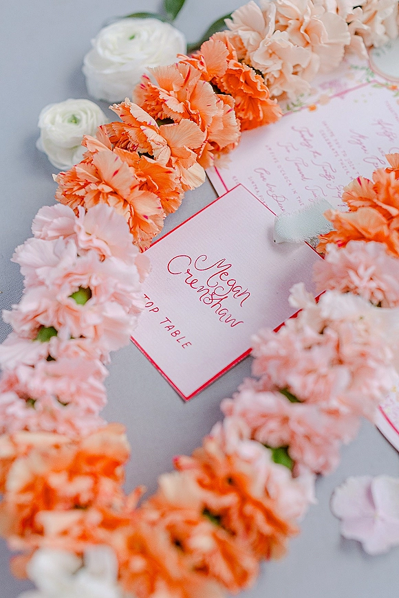 Wedding invitation suite with calligraphy wedding invitations, RSVP card, ribbon and carnations in a floral garland on a gray tabletop