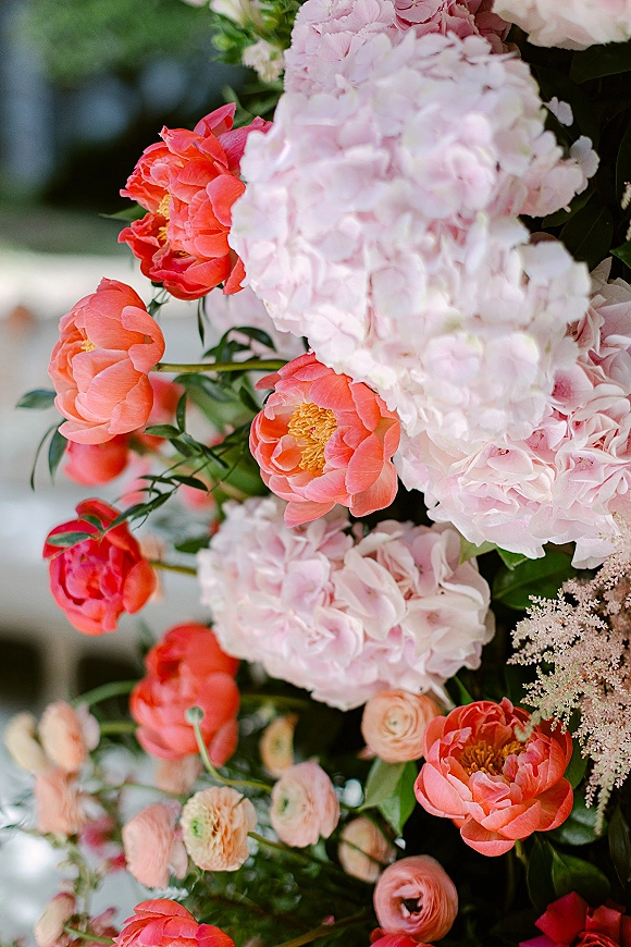 Wedding floral arrangement with peony wedding flowers in coral and pink, featuring hydrangea, ranunculus, and greenery in a soft garden bokeh background