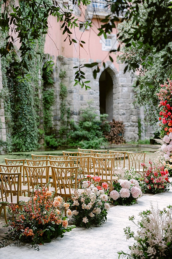 Ceremony aisle decor with outdoor ceremony aisle flowers lining wood chairs, peony and rose florals in an ivy-walled garden courtyard